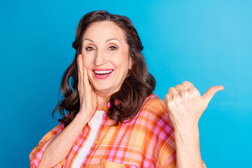 Cheerful mature woman in bright plaid shirt pointing with hand, expressing joy with vibrant smile...