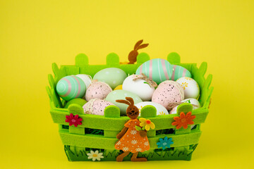 Colorful Easter eggs in a green basket on a yellow background. Easter Feast
