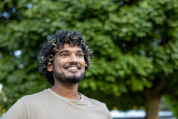 A young man with curly hair and a short beard is smiling and looking up against the bokeh...