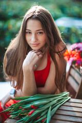Naklejka premium Adorable girl holding bouquet of red tulips in outdoor cafe