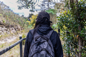 Young woman traveler with cap and travel suitcase hiking on a trail in the mountains