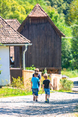 Obraz premium Group of Young Kids Walking on a Rural Path Near Old Wooden Houses on a Sunny Day