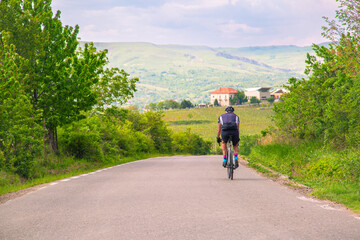 Cyclist Enjoying a Scenic Ride Through a Rural Road Surrounded by Lush Greenery and Hills
