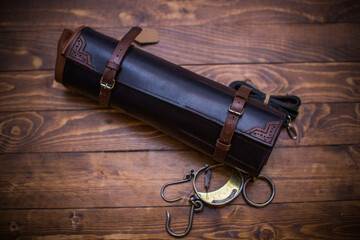 Elegant Brown Leather Roll With Buckles on Wooden Surface and Vintage Tools