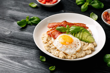 Savory Oatmeal breakfast with sunny side up fried egg, bacon and avocado. Healthy food