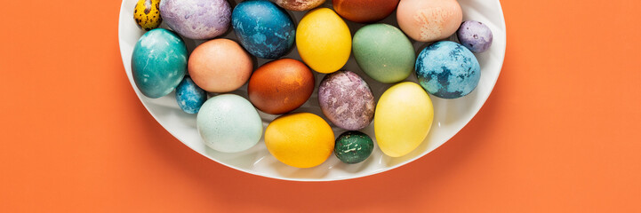 Top view of oval dish with dyed natural dyes Easter eggs on orange background, Happy Easter