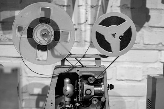 Vintage reel-to-reel film projector against a brick wall background.  Classic cinema. Black and white. 
