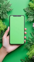 Mobile Technology with Green Screen and Greenery: A human hand elegantly holds a modern phone with a vibrant green screen, framed by lush green foliage against a matching background.