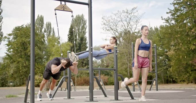 Young people exercising using parallel bars and outdoor gym equipment in a green park setting
