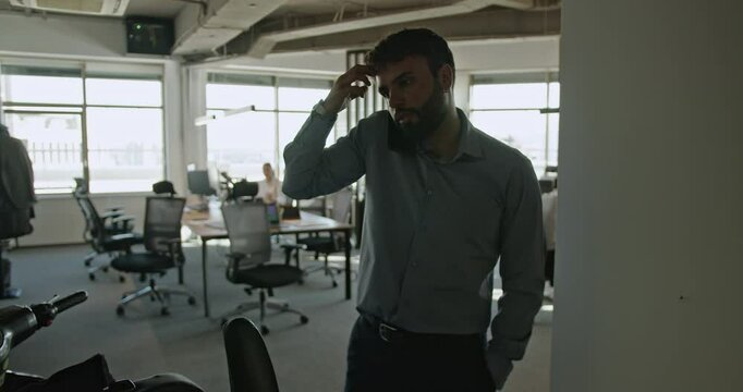 Businessman talking on the phone, looking concerned and scratching his head. He then joins a female colleague, and they review blueprints.