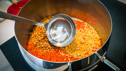 Raw red lentils, green lentils and short pasta, scoop are into the pot.