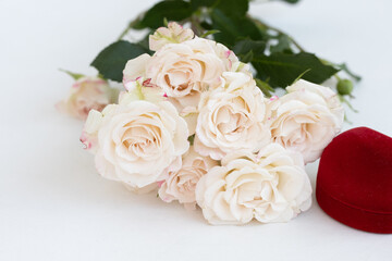 Bouquet of delicate, cream-colored  roses surrounded by lush, green foliage, adding to the overall natural and romantic aesthetic. A red velvet box in the foreground. Wedding, anniversary, .