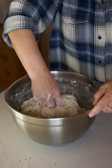 A woman kneads dough with her hands in a bowl.