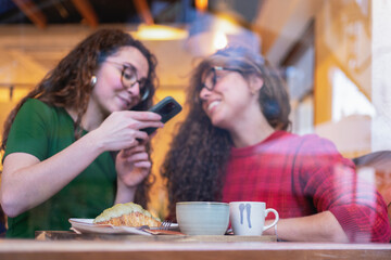 Two friends laughing and looking at a smartphone in a cozy cafe