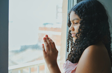 Young woman looking out the window touching the glass with her hand