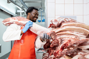 Slaughterhouse worker carrying pork meat for processing in cold storage butchery shop.