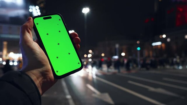 Pov view male hand holding modern smartphone keylight green screen gadget in street at night, camera locked on cell phone chroma key display, bokeh city illumination in evening, copy space
