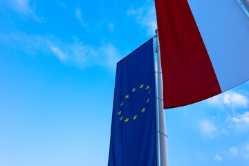 Polish and European flags flying on a mast against a blue sky background. Photo taken in the late afternoon, natural light