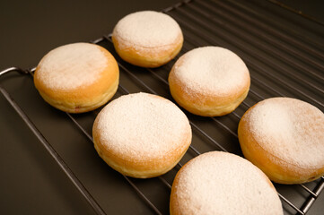 Freshly baked golden donuts dusted with powdered sugar rest on a cooling rack, ready to be enjoyed. A mouthwatering visual that evokes the joy of sweet treats and homemade baking.