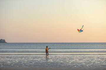 Evening at the beach with a boy flying a kite. Silhouette against sunset over the sea, evoking freedom, play, and peaceful coastal atmosphere.