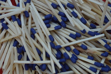A close up of a set of wooden matches arranged on an isolated dark background. The match heads are blue in color and the wooden sticks have a natural texture. The sticks are ready to use.