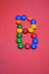 colored chocolate coated candy alphabet on pink background B