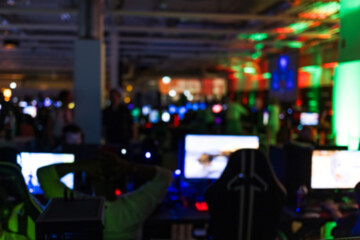 Blurred out of focus indoor space with computer screens and neon lights during esports tournaments...