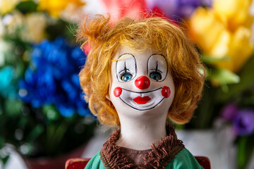 antique clown doll with orange hair and glass eyes isolated on spring flower background