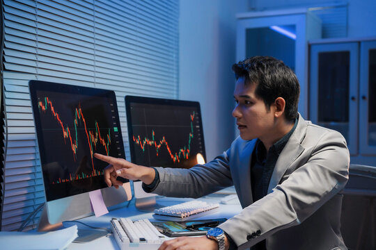 Focused stockbroker reviewing cryptocurrency market trends, tracking financial data on computer screen during late night work session in modern office environment