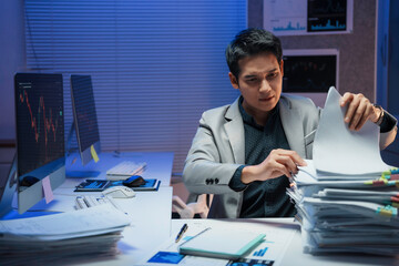 Professional businessman reviewing financial data, working late with intense concentration, illuminated by blue computer screen light in modern office setting