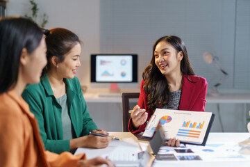 Asian businesswomen reviewing financial charts, collaborating on company performance data during strategic meeting, sharing insights in professional workspace