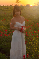 Beautiful blonde girl in a white dress on the poppy field at sunset