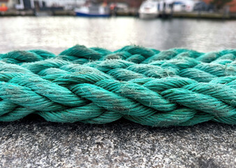 Thick green twined frayed rope against a blurred maritime background