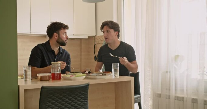 Two Caucasian men enjoy a healthy breakfast together in their modern apartment, discussing their day ahead.