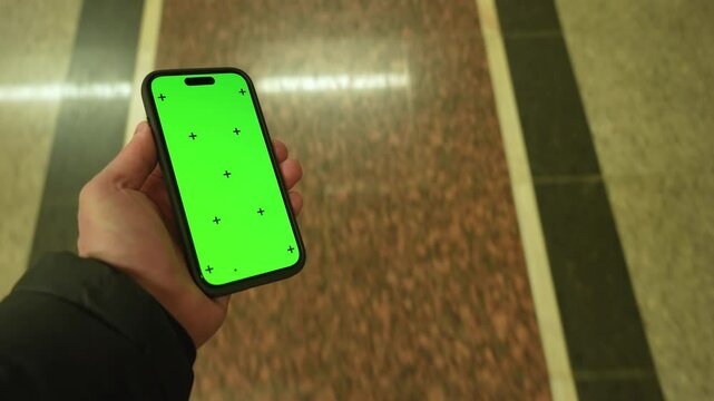 Pov view male hand holding modern smartphone keylight green screen gadget walking in street at night, camera locked on cell phone chroma key display, subway metro station, copy space