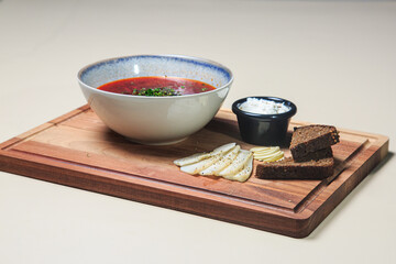 a wooden serving tray with a bowl of vibrant red borscht soup in the center. The soup is garnished with fresh chopped herbs, likely dill or parsley, which adds a nice pop of color and freshness.