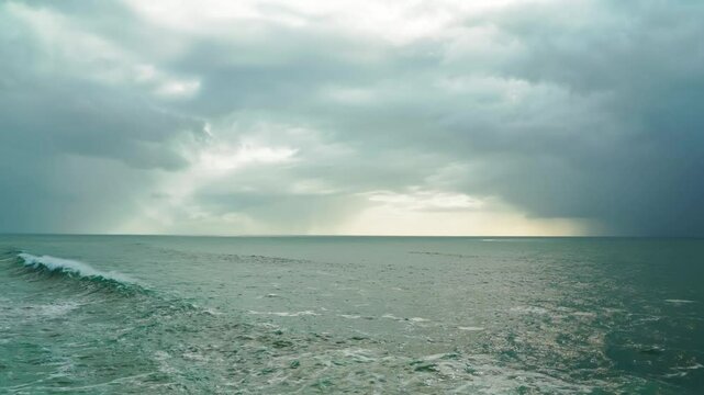 Dark storm clouds loom over the vast ocean, with distant rain showers visible on the horizon. Concept of natures unpredictability and approaching storm