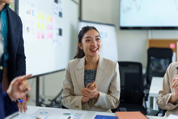 Professional asian businesswoman smiling confidently, collaborating with team members, reviewing data charts in contemporary workplace setting