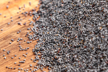 Scattered poppy seeds on a rustic wooden background. Black tiny particles. Raw baking ingredient. Macro. 