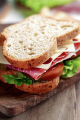 Whole grain bread sandwich with cured ham, Kumato tomato, Swiss cheese and fresh lettuce on a wooden board