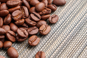 Roasted Arabica coffee beans scattered on a textured woven mat. Brown fragrant grains with natural cracks. Aromatic drink ingredient. Macro. 