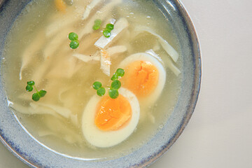 The image shows a bowl of clear broth-based soup, likely a chicken noodle soup. 