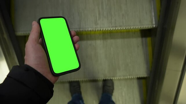 Pov view male hand holding modern smartphone keylight green screen gadget walking in street at night, camera locked on cell phone chroma key display, subway metro station escalator, copy space