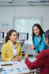 Fototapeta premium Professional Asian businesswomen collaborating, reviewing marketing performance charts in sleek corporate workspace, strategizing company growth and financial planning