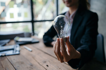 Businesswoman grasping glowing light bulb, symbolizing innovative thinking and creative potential within corporate workspace