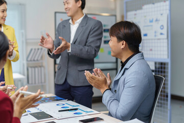 Asian businesspeople clapping hands after a successful presentation during a meeting in a modern office, celebrating business achievements and accomplishments