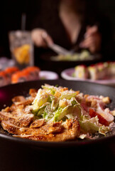 Close-up Caesar salad with chicken breast, dinner in restaurant with a girl on background.