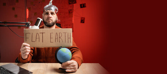 Strange man in a protective foil cap holding banner with Flat Earth message. filming commercial...