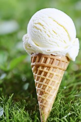 Vanilla ice cream cone in grass outdoors, blurred green background