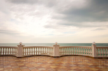 Terrace by the sea with railings and columns against a dramatic sky. A sad and lonely mood.